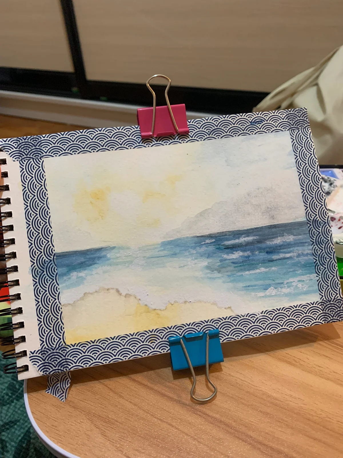 Sketchbook painting of blue sea and pale sand beneath a softly lit sky.