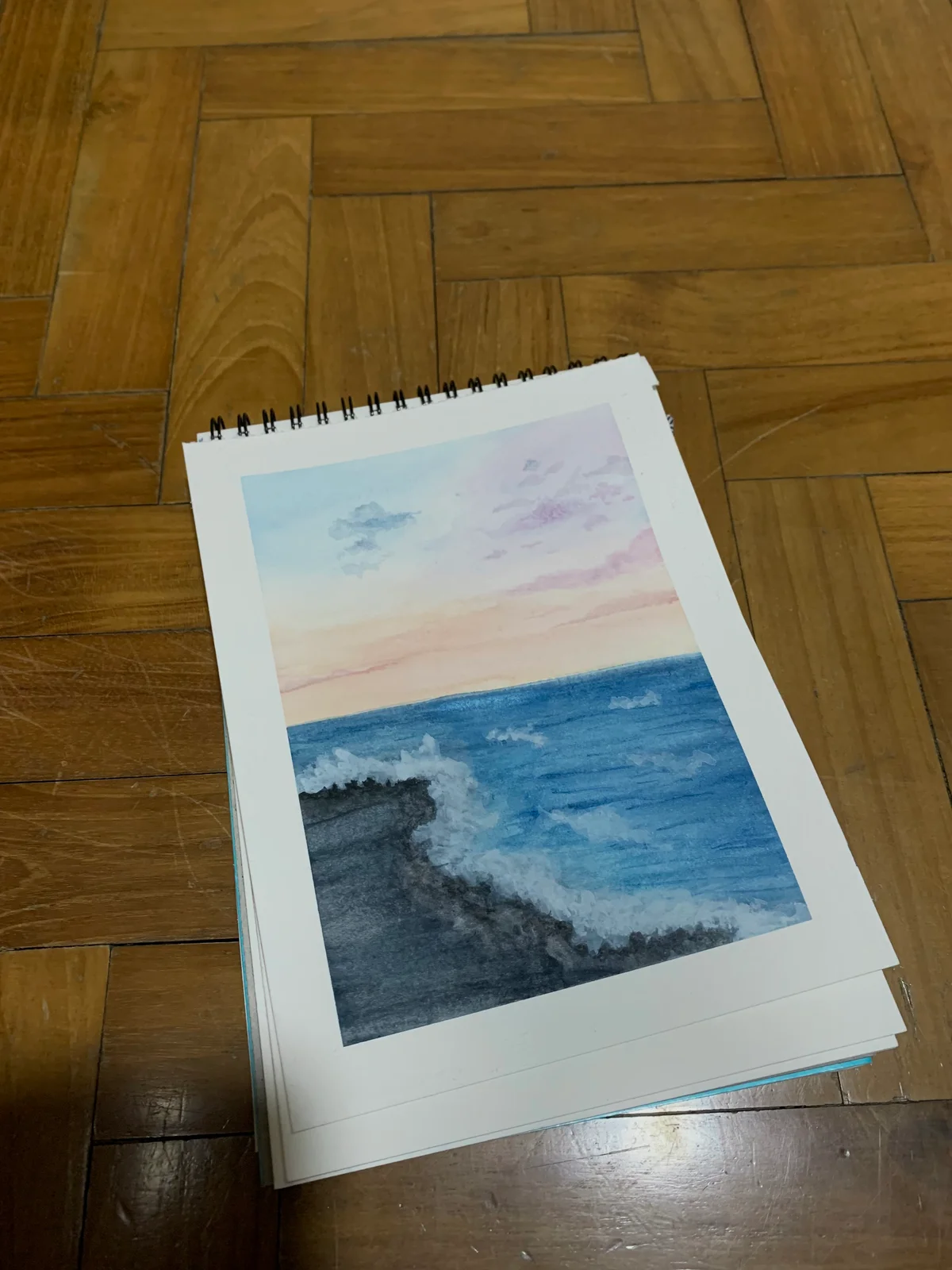 Sketchbook painting of waves meeting a dark rocky coast beneath a pastel sky.