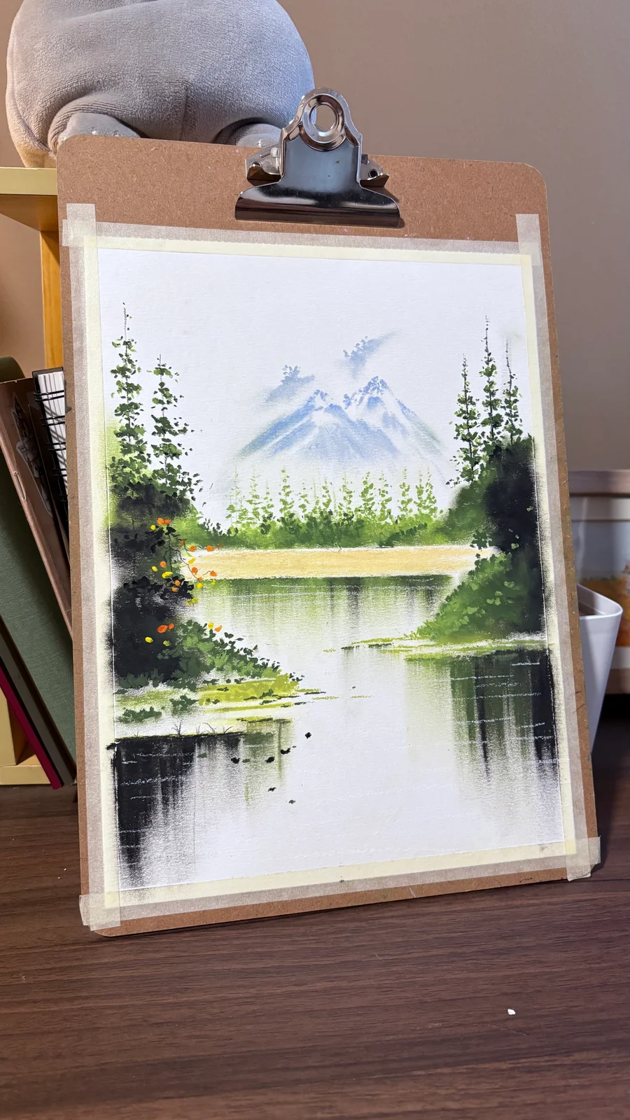 Painting of a snowy mountain above a lake, framed by evergreen trees.